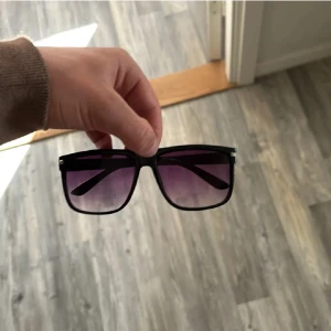 Liknar raybans boyfriend  - Snygga solglasögon med svart, fyrkantig båge och lila tonade glas. Perfekta för att ge din look en cool vibe och skydda ögonen mot solen. Passar dig som gillar stilrena accessoarer med en twist.