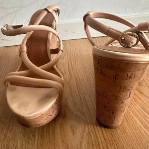 Ljusrosa sandaler med kilklack - Snygga sandaler i ljusrosa med korsade remmar och justerbart spänne. Skorna har hög kilklack och plattform i kork-look som ger extra höjd och somrig vibe. Perfekta för dig som vill sticka ut med en trendig och bekväm stil