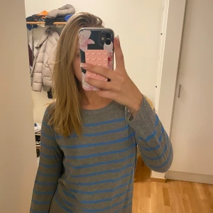 Gråblå randig stickad tröja - Säljer en grå stickad tröja med blå horisontella ränder. Tröjan har rund halsringning och långa ärmar, perfekt för dig som gillar en enkel men ändå snygg stil. Skön passform och passar till det mesta i garderoben.