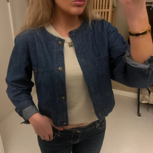Mörkblå croppad jeansjacka - Säljer en mörkblå croppad jeansjacka med rund halsringning och knappar framtill. Jackan har två bröstfickor och långa ärmar som kan vikas upp för en chill look. Perfekt att slänga över en t-shirt för en avslappnad vibe❤️