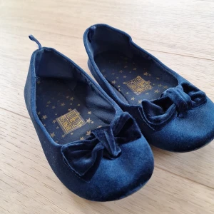 Mörkblå sammet ballerinaskor med rosett - Snygga mörkblå ballerinaskor i mjuk sammet med rund tå och dekorativ rosett framtill. Skorna har platt sula och är perfekta för dig som gillar en klassisk och söt stil. Insidan har ett stjärnmönster i guld för extra detalj. Storlek 34