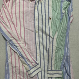 Randig skjorta Polo Ralph Lauren S - Färgglad randig skjorta från Polo Ralph Lauren i custom fit. Skjortan har långa ärmar, knappar framtill och klassisk krage. Färgerna är rosa, blå, grön och vit i olika breda ränder. Broderad logga på bröstet. Perfekt för dig som gillar preppy och unik stil.