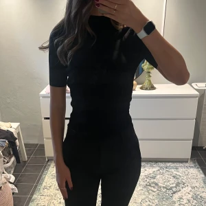 Svart bodysuit med öppen rygg - Säljer en svart, tight bodysuit med hög hals och korta ärmar. Baksidan har en stor, öppen rygg som ger en snygg och edgy look. Perfekt att styla med både jeans och kostymbyxor för en clean vibe.