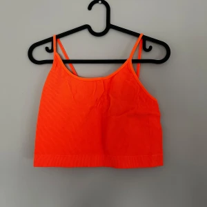 Neonorange ribbad linnetopp - Snygg neonorange linnetopp med smala axelband och ribbad struktur. Perfekt för att sticka ut och ge färg till din outfit. Lite träningsmaterial 