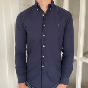 Polo Ralph lauren skjorta  - Säljer denna riktigt snygga mörkblåa Ralph lauren skjorta! Den är i mycket bra skick enda defekten är loggan som är något urtvättad annars mycket bra skick, storlek S modell slim fit, den är 72 cm lång och 48 cm bred under armhålorna, jag på bilderna är 184 cm lång och väger 82 kg, hör gärna av dig vid frågor!
