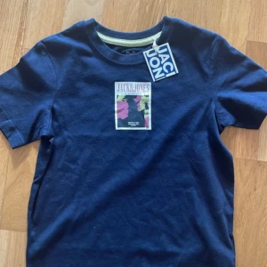 Mörkblå t-shirt Jack & Jones - Snygg mörkblå t-shirt från Jack & Jones med coolt tryck på bröstet i rosa, gul och svart. Klassisk rund hals och korta ärmar.