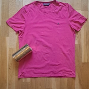 Rosa t-shirt från Morris Stockholm - Snygg rosa t-shirt från Morris Stockholm i storlek M. Klassisk rund hals och korta ärmar. T-shirten har en liten broderad logga på bröstet och är gjord i mjuk bomull som känns skön mot huden. Perfekt för dig som gillar färg och stil.