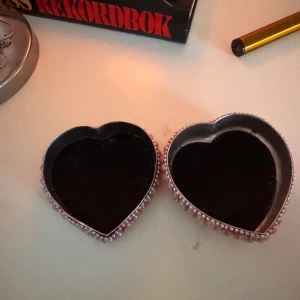 Hjärtförmatt smyckesask med pärlor - Superfin hjärtformad smyckesask dekorerad med ljusrosa pärlor och glittriga detaljer. Locket har en stor röd sten i mitten omgiven av små strasstenar. Perfekt för att förvara dina favoritsmycken eller som presentask. Använd och har lite skador men absolut inget man märker!💕💕