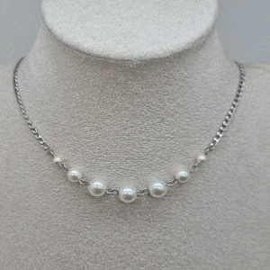 Silverhalsband med pärlor - Stilrent halsband med silverfärgad kedja och sju vita pärlor i olika storlekar framtill. Kedjan är tunn och har ett klassiskt lås. Perfekt accessoar för att lyfta din outfit med en touch av elegans och trend.