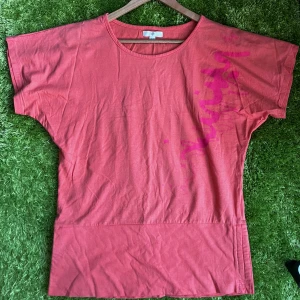 Rosa loose topp med tryck - En oversized rosa topp i mjuk bomull. Toppen har korta ärmar, rund halsringning och ett coolt rosa tryck längs ena axeln. Perfekt för en avslappnad och trendig look.