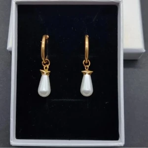 Guldiga örhängen med droppformad pärla - Snygga örhängen i guldton med droppformade vita pärlor som hänger från små ringar. Klassisk och elegant design som ger en lyxig känsla. Perfekta för att lyfta vilken outfit som helst.