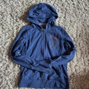 Blå hoodie från Polo Jeans Company - Snygg blå hoodie från Polo Jeans Company by Ralph Lauren med dragkedja och broderad logga på bröstet. Tröjan har huva, långa ärmar och två fickor framtill. Perfekt för en chill och sportig look.