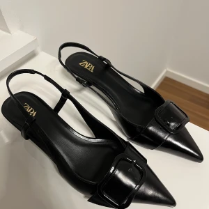 Svarta kitten heels - Stilrena svarta kitten heels från Zara med spetsig tå och elegant spänndetalj framtill. Skorna har smal rem runt hälen och låg klack. 