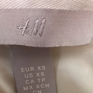 Vit omlottklänning från H&M XS - Supersnygg vit omlottklänning från H&M i storlek XS. Klänningen har v-ringning, är ärmlös och har ett bälte med spänne i midjan. Perfekt för sommarens alla tillfällen och ger en fräsch och stilren look.