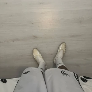 Vita adidas fotbollsskor utan snörning - Säljer ett par vita adidas fotbollsskor med klassiska tre ränder i silver på sidorna. Skorna har en strumpliknande passform utan snörning och är tillverkade i syntetmaterial med textildetaljer upptill. Perfekta för dig som vill ha en clean look på planen.