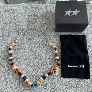Ying yang pärlhalsband från TwoJeys - Unikt halsband från TwoJeys med pärlor i vitt, grönt, blått, rött och gult. Dekorerat med stjärnor, peace-symboler, eldiga hjärtan och blå stjärnhänge. Silverfärgad kedja och lås med extra stjärndetaljer. Perfekt statement-piece för dig som gillar färg och coola detaljer.