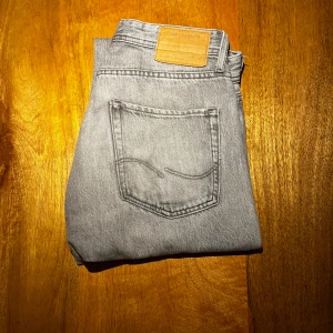 Grå relaxed jeans från Jack & Jones - Snygga grå jeans från Jack & Jones i relaxed fit-modell Chris. Klassisk femficksdesign, raka ben och normal midja. Jeansen är tillverkade i mjukt bomullstyg och har en stilren, ljusgrå tvätt som passar till det mesta. Har tyvärr ett hål i skrevet som jag själv lagat diskret och är även slitstarkt och tål lite påfrestning utan att spräckas igen. Vid funderingar är det bara att kontakta mig jag är ärlig och rak med svar.