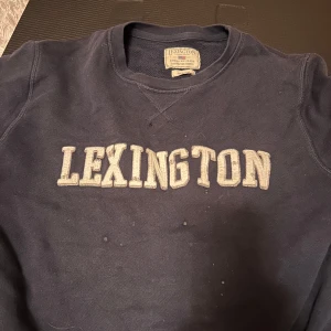 Mörkblå Lexington sweatshirt M - Klassisk mörkblå sweatshirt från Lexington med broderad logga i vitt framtill. Tröjan har rund halsringning och långa ärmar, perfekt för en avslappnad och stilren look. Tillverkad i mjuk bomull för extra komfort.