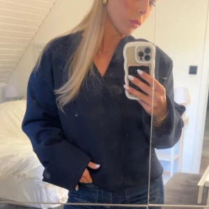 Mörkblå cardigan/kappa med v-ringning - Snygg mörkblå kavaj med v-ringad hals och dubbla knappar framtill. Jackan har en loose passform och långa ärmar med breda muddar. Perfekt att styla med jeans för en chill och trendig look. Från Gina ✨