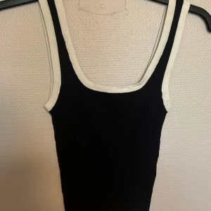 Svart ribbad linnetopp från Divided - Svart ribbad linnetopp från Divided med vita kontrastkanter runt hals och ärmhål. Tidlös och enkel design som är lätt att matcha. Perfekt för lager-på-lager eller sommarens varma dagar.