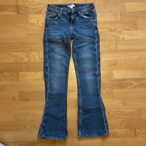 Blå bootcut jeans från Gina Tricot - Snygga blå jeans från Gina Tricot i storlek 146. Modellen har klassisk femficksdesign, normalhög midja och bootcut-ben. Jeansen är i mjukt denimtyg med lätt slitningar och kontrastsömmar. Perfekta för en avslappnad och trendig look.