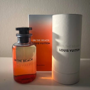 Louis Vuitton On The Beach parfym - Lyxig parfym från Louis Vuitton, On The Beach, med en snygg cylinderformad glasflaska i orange och transparent ton. Svart lock och stilren förpackning med vit och orange gradient. Perfekt för dig som gillar exklusiva dofter och snygg design.