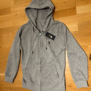 Grå zip hoodie från Polo Ralph Lauren - Säljer en grå polo ralph lauren zip hoodie i storlek S med qr scan hoodien är i nyskick
