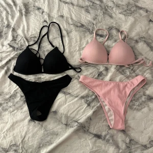 Svart och ljusrosa bikini-set - Två snygga bikinis säljes! Ena setet är helsvart med trekants-bh och smala axelband, andra är ljusrosa med ribbad struktur och matchande trosor. Båda har klassisk bikini-modell och passar perfekt för strandhäng eller poolparty. Båda för 40kr