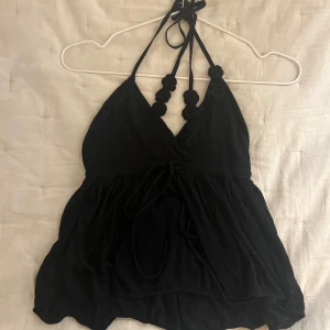 Svart  halterneck topp - Supersöt svart stickad topp från bikbok med halterneck och virkade blommor på banden. Toppen har knyt i nacken och under brösten. Perfekt till fest och sommar. Oanvänd med prislapp.