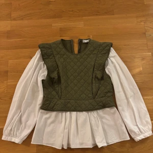 Olivgrön quiltad väst med volang - Säljer en olivgrön quiltad väst från ZARA med markerade axlar och volangdetaljer. Västen har en snygg struktur med rutmönster och dragkedja i ryggen. Perfekt att styla över en skjorta eller klänning för en trendig lager-på-lager-look.