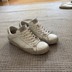 Vita sneakers från Crime London - Snygga vita sneakers från Crime London med klassisk låg profil och rund tå. Skorna har snörning och är gjorda i skinn med detaljer i mocka. Perfekta för dig som gillar en clean och stilren look med streetkänsla.