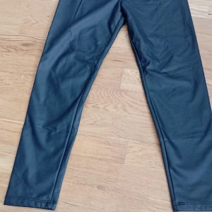 Svarta byxor i skinnimitation LC Waikiki - Snygga svarta byxor i skinnimitation från LC Waikiki. De har resår i midjan för extra komfort och en rak passform. Perfekta för dig som vill ha en cool och trendig look. Passar till många olika outfits och är lätta att matcha.