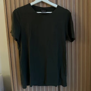 T-shirt  från Oscar Jacobson - Snygg mörkgrön t-shirt från Oscar Jacobson i mjuk bomull. Klassisk rund hals och korta ärmar, perfekt för en clean och enkel stil. Passformen är normal och materialet känns skönt mot huden. En basic tee som funkar till allt.