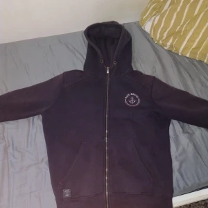 Mörkblå hoodie från Race Marine - Säljer en mörkblå hoodie från Race Marine med dragkedja och huva. Tröjan har ett ankare-tryck på bröstet, två stora fickor fram och mysigt fleecefoder på insidan. Snygga röda detaljer på insidan och klassisk passform. Perfekt för chill eller skola, lite användning syns på den och urtvättad 