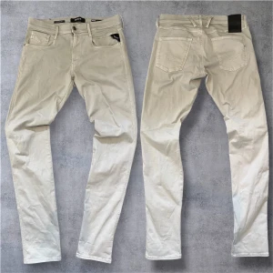 Grå Replay Anbass Hyperflex  - Knappt använda Snygga beige Replay Anbass Hyperflex jeans med klassisk femficksdesign och svarta detaljer på fickan. Jeansen är i stretchigt material för extra komfort och har en slim passform. Perfekta för dig som gillar stilrena och ljusa jeans med modern känsla.