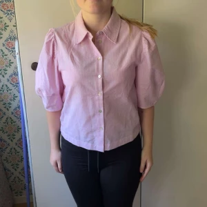 Rosa randig skjorta Carin Wester - Säljer en rosa och vit randig skjorta från Carin Wester i storlek 40. Skjortan har puffiga korta ärmar, klassisk krage och knäppning framtill. Perfekt för dig som gillar en trendig och söt look med lite volym på axlarna.