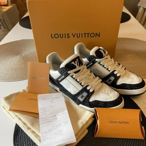 Louis Vuitton svartvita sneakers - Exklusiva Louis Vuitton sneakers i svart och vitt skinn med klassiskt monogrammönster och tydliga LV-detaljer. Snygg design med rund tå, snörning och platt sula. Perfekta för dig som vill sticka ut med lyxig streetstyle.
