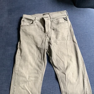 Replay ljusgrå jeansbyxor - Säljer ett par ljusgrå jeans från Replay med klassisk femficksdesign och snygga detaljer på bakfickan. Jeansen har rak passform och är tillverkade i mjukt bomullsmaterial med en hint av stretch för extra komfort. Perfekta för en clean och stilren look.