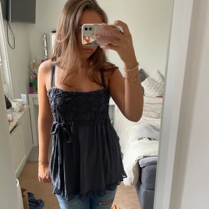 Mörkgrå topp med rosett - Säljer en snygg topp med rosett i midjan. Toppen kan bäras både med axelband eller axelbandslös. Materialet känns lätt och flowy, perfekt till jeans eller kjol!