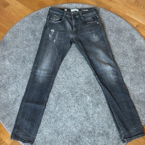 Replay Anbass grå slim jeans herr - Snygga Replay Anbass jeans i grå tvätt med slitningar och slim fit passform. Klassisk femficksmodell med dragkedjegylf och coola detaljer. Perfekta för dig som gillar en modern och avslappnad stil.