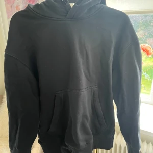 Svart hoodie från Sail Racing - Svart hoodie från Sail Racing med klassisk känguruficka och snörning i huvan. Tröjan har en relaxed passform och är tillverkad i mjuk bomullsmix. Perfekt för chill dagar eller när du vill ha en clean och enkel stil.