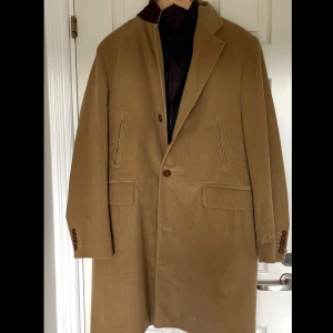 Vintage beige manchesterrock från Gant med insydd jacka - Säljer en vintage beige rock i manchester med klassisk krage och knäppning framtill. Jackan har två fickor med lock och två snedställda bröstfickor. Insidan har en insydd jacka som är avtagbar med innerfoder och dragkedja för extra värme. Perfekt för höst och vinter!