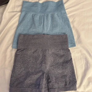 Två par seamless träningsshorts - Säljer två par seamless träningsshorts med hög midja, ett par i ljusblått och ett par i mörkgrått. Båda har ribbad midja och ventilerande mesh-detaljer längs sidorna. Perfekta för gymmet eller löpning, sitter tight och följsamt mot kroppen. 100kr för båda