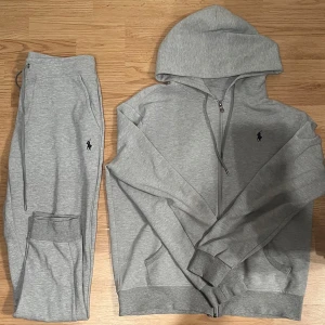Grå hoodie från Polo Ralph Lauren - Snygg grå hoodie från Polo Ralph Lauren med dragkedja och huva. Klassisk logga broderad på bröstet, ribbade muddar och fickor framtill. Perfekt för chill dagar eller när du vill ha en clean och enkel stil.