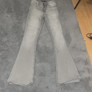 Grå flared jeans från New Yorker strl 34 - Snygga grå jeans från New Yorker flared fit med klassisk femficksdesign och smal passform upptill som går ut i breda ben. Jeansen har en cool, ljusgrå tvätt och är tillverkade i mjukt jeansmaterial. Perfekta för dig som gillar retrovibbar och statement-plagg. Dom e långa och till för långa tjejer med smala ben 