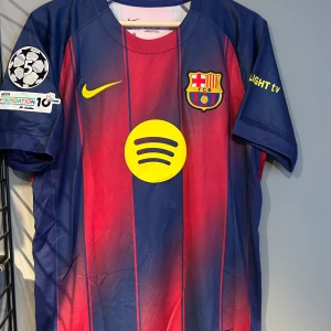 FC Barcelona Pedri matchtröja Nike - Säljer en officiell FC Barcelona matchtröja med Pedri #8 på ryggen. Tröjan är kortärmad, har klassiska blå och röda vertikala ränder, gula detaljer och klubbmärke på bröstet. Materialet är lätt och andas, perfekt för fotboll. Sponsorloggor från Spotify och UNHCR. Helt ny med tagg en replika 