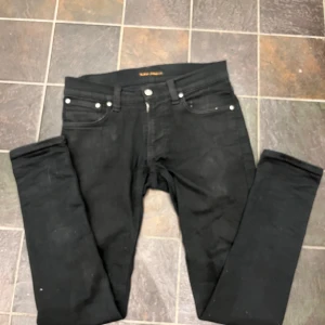 Svarta  jeans från Nudie Jeans - Svarta jeans från Nudie Jeans med klassisk femficksdesign och svarta sömmar. Byxorna har en stilren look med svart patch bak i midjan och Nudie Jeans-logga på bakfickan. Perfekta för dig som gillar lite mer sköna jeans  ganska dåliga bilder skriv om du vill ha mer bilder 