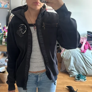 Svart hoodie från G-Star RAW med brodyr - Svart hoodie från G-Star RAW med stor broderad logga och patchar på ryggen, samt brodyr på bröstet. Tröjan har dragkedja, huva med snörning och coola detaljer som bröstficka med dragkedja. 