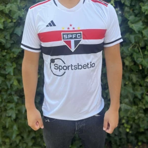 SPFC vit fotbollströja från Adidas - Snygg vit fotbollströja från Adidas med SPFC-logga på bröstet och Sportsbet.io sponsortryck. Tröjan har röda och svarta horisontella ränder över bröstet och ryggen, samt korta ärmar med svarta detaljer. Tillverkad i lätt och ventilerande polyester.Nypris:600kr GORILLAPRICE:230kr																																											SKICK:10/10 med tagg kvar                    KVITTO MEDKOMMER