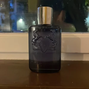 Parfums de Marly Sedley Eau de Parfum - Säljer en lyxig Parfums de Marly Sedley Eau de Parfum, 125 ml. Flaskan är mörkblå med silverfärgat lock och har en elegant, rektangulär form med relief av två hästar och sköld. Perfekt för dig som gillar exklusiva dofter och snygg design.